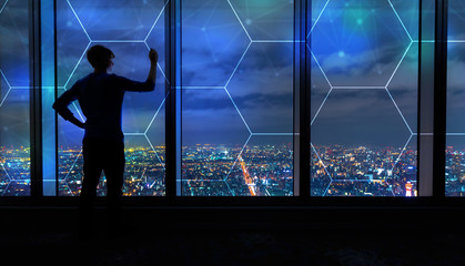 Fototapeta na wymiar Hexagon Grid with man writing on large windows high above a sprawling city at night
