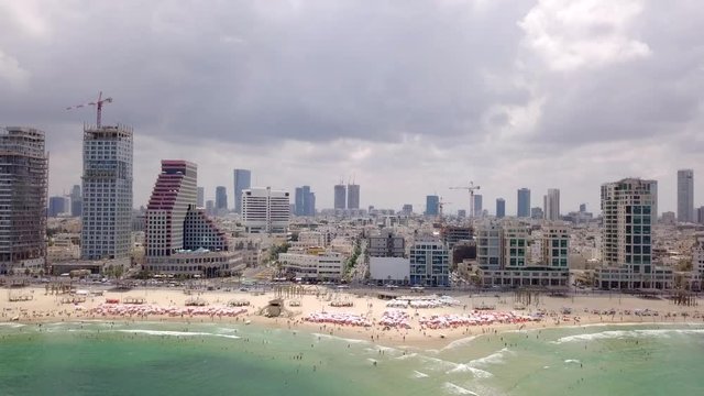 Aerial footage of Tel Aviv's skyline along the coastline with people at the beach on a summer's day