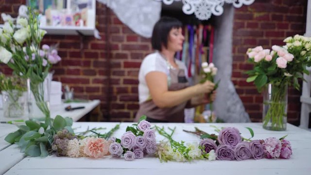 Defocused professional caucasian female florist master preparing and selecting rose branches for flower bouquet arrangement in floral design studio. Floristry, handmade and small business concept