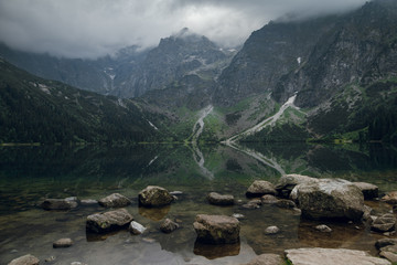 Scenic view of beautiful foggy rocky mountains and green forest with a reflection in a lake. Stony shore on Morskie Oko. Travel concept. High Tatras, Poland © WellStock