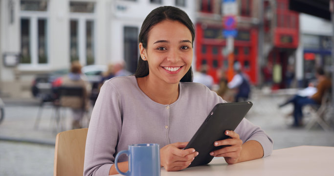 Happy Latina female using her tablet outside at a cafe 