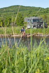 Fototapeta premium A man casts a fly in front of his Land Rover.