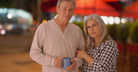 Mature Caucasian wife and husband on sidewalk looking seriously at camera
