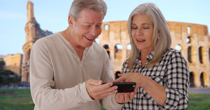 White elderly couple look through photos on smartphone near Colosseum in Rome