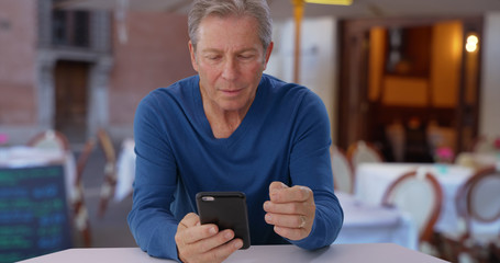 Caucasian male senior uses smartphone while sitting at restaurant in Europe
