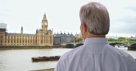 Older white man in London looks on at Big Ben over River Thames