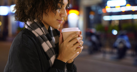 Close up of cute African female enjoying coffee on urban street at night