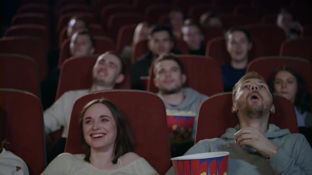 Young people laughing at cinema theater. Joyful people watching amusing comedy. Cheerful people smiling at movie theatre watching comedy film in slow motion. Friends spend weekend in cinema