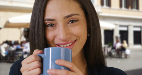 Close up of pretty Latin woman enjoying cup of coffee outdoors in daytime