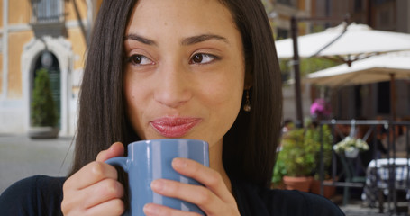 Cute pensive Latina woman looking around and drinking coffee outdoors