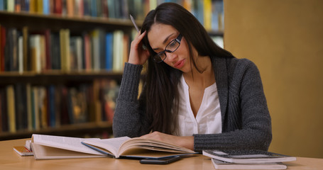 Pretty Hispanic woman with glasses studies at the library