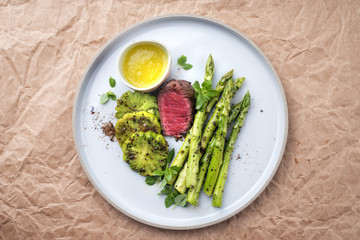 Modern barbecue dry aged sliced fillet steak with green asparagus and tomatoes as top view on a plate with copy space
