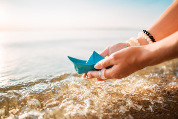 Girl holds a blue paper boat in the hands on a blue sea background. Summer by the sea