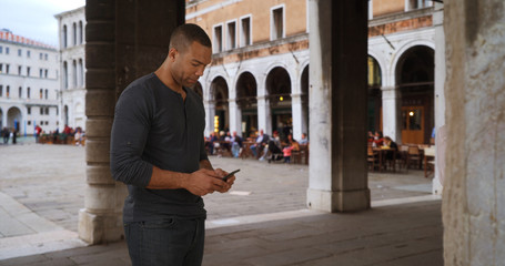 Attractive African male tourist texting friend in urban setting Italy