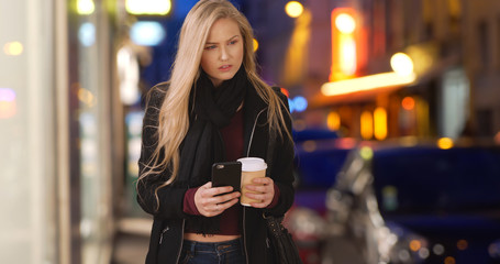 Modern white female using smartphone and drinking coffee in city at night