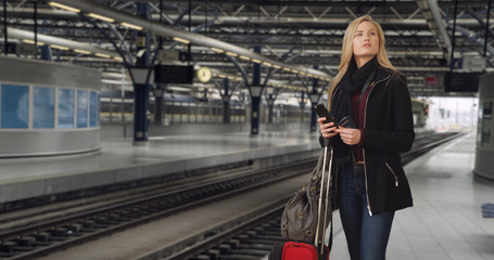 Traveling young white female waits for train to arrive at station