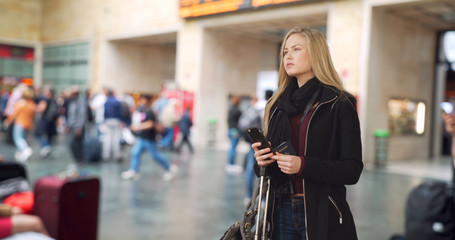 Traveling blonde white female checks smartphone at busy airport 