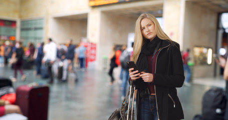 Traveling blonde white female checks smartphone at busy airport 