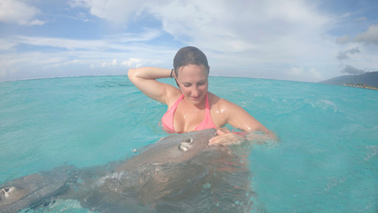 CLOSE UP: Happy young woman cooling off in ocean pets two friendly grey sea rays