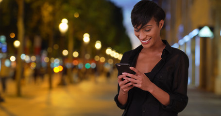Millennial black woman tourist checks emails on phone at the Champs-Elysees 