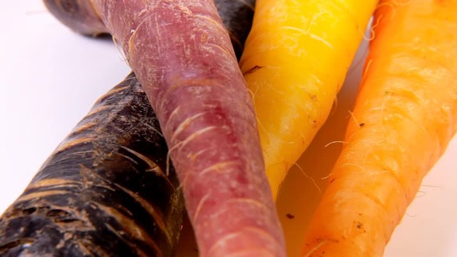 A bunch of carrots (not the most common variety, but with yellow and violet colors) on a rotating surface. Mix of fast paced shots for product presentation.
