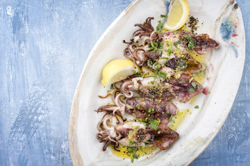 Traditional barbecue Greek calamari with herb and lemon as top view on a plate