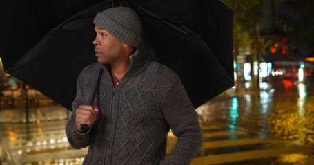 African male holding umbrella outside on rainy night in the city
