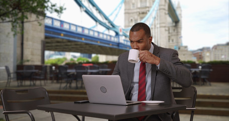 African businessman working on laptop while drinking coffee at London cafe 