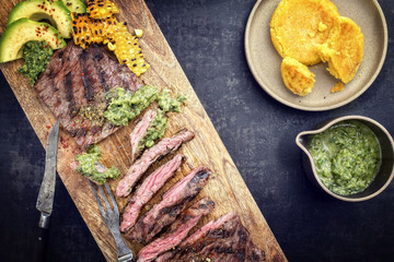 Barbecue dry aged wagyu flank steak with arepas corn, and chimichurri sauce as top view on a cutting board