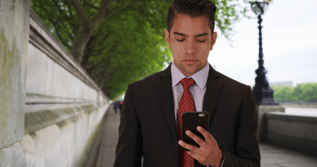Latino businessman text messaging on mobile phone by River Thames