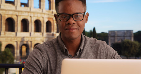 Portrait of happy African American man sitting with laptop near Coliseum
