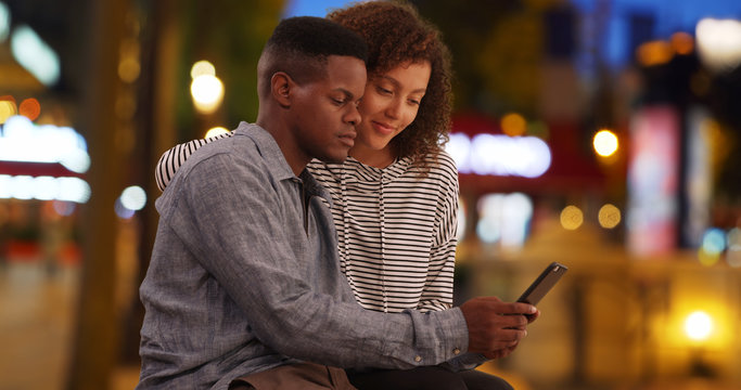 Cute African American couple relax on Champs-Elysees avenue using smartphone