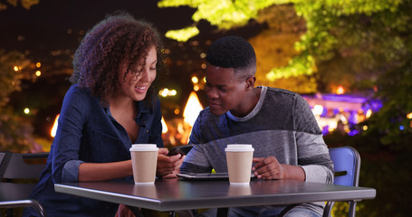 Black male and female meeting for coffee at night use tablet computer