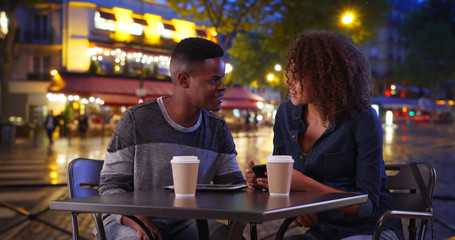 African American man and woman drink coffee and use smartphone on Paris street