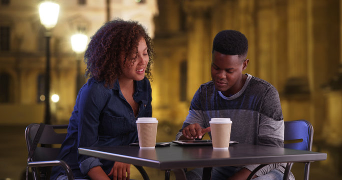 African American man and woman sit outside using touchscreen devices - Powered by Adobe