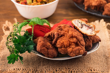 Fish in dough, fried in oil until brown, one piece cut in a plate with slices of tomato, decorated with basil  and parsley branches.