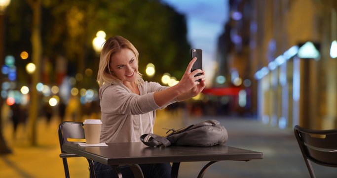 Peppy female taking selfie on phone while sitting at table on Champs-Elysees