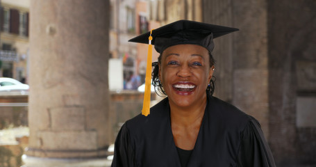 Portrait of senior black woman in graduation gown smiling and cheering