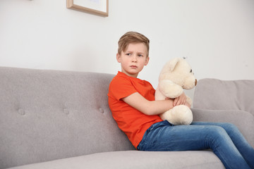 Little autistic boy sitting on sofa with toy at home