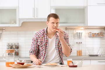 Fototapeta na wymiar Young man eating tasty toasted bread with jam at table in kitchen