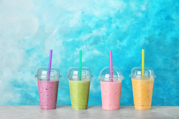 Plastic cups with smoothies on table against color background