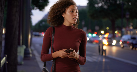 Fototapeta na wymiar Stylish black woman texting on city street in evening
