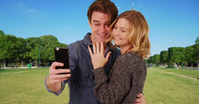 Newly engaged couple taking a selfie in front of the Eiffel Tower smiling