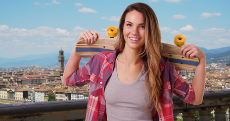 Happy Caucasian woman in Florence holding skateboard on her shoulders