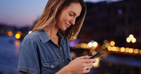 Smiling Caucasian woman using mobile phone outdoors at night