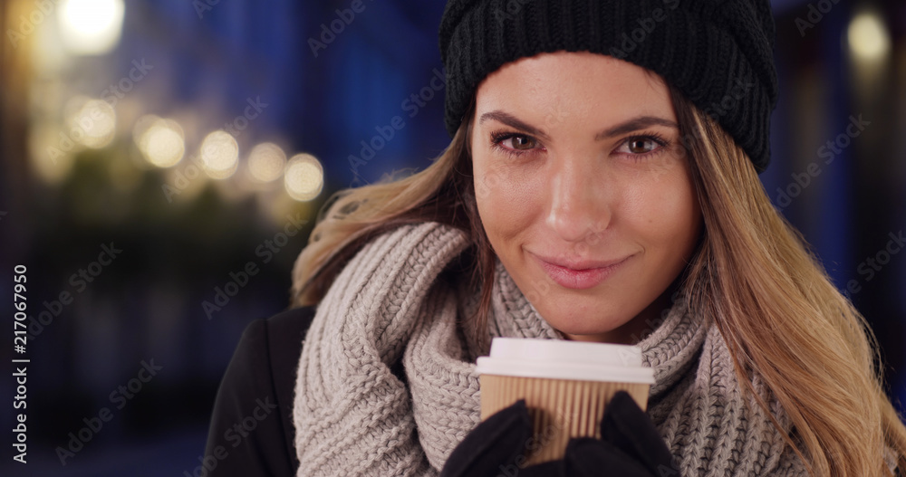 Wall mural Cheerful female in cozy hat and scarf enjoying hot coffee outside