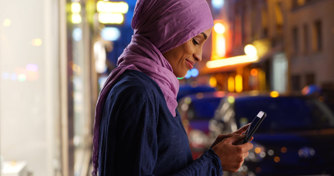 Young Muslim woman on urban street at night texting
