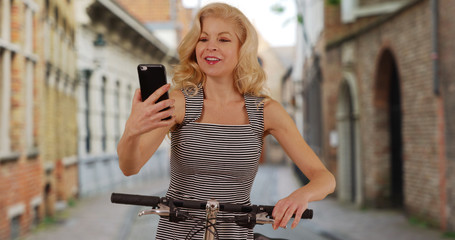 Tourist woman rides bike through Bruges Belgium using map on mobile phone