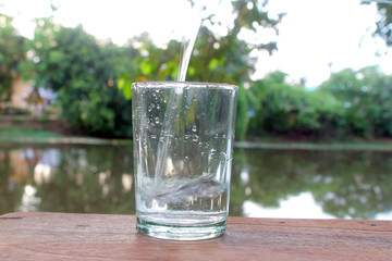 Close up pouring purified fresh drink water from the bottle on wooden table with nature background