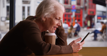 Happy senior woman receives good news via text while waiting in coffee shop